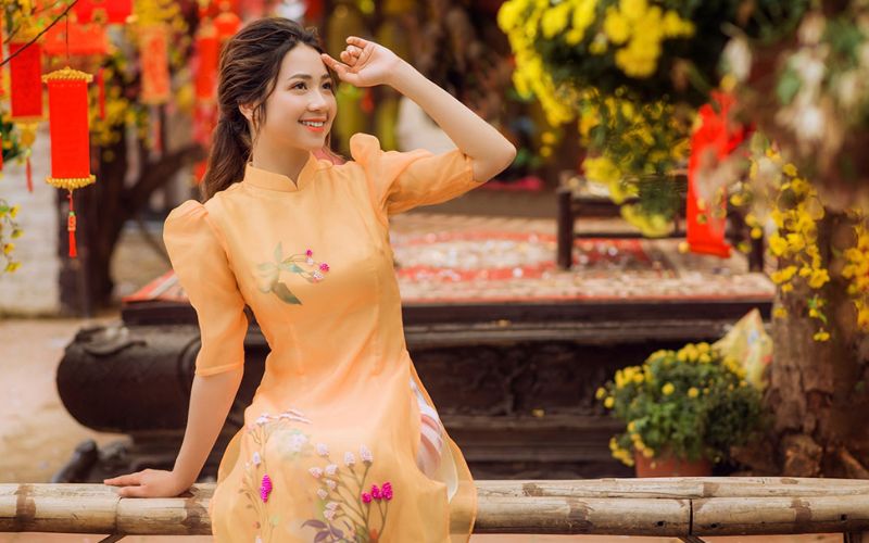 Posing for a Tet (Lunar New Year) photo in a traditional Ao Dai dress, sitting gracefully beside apricot blossoms