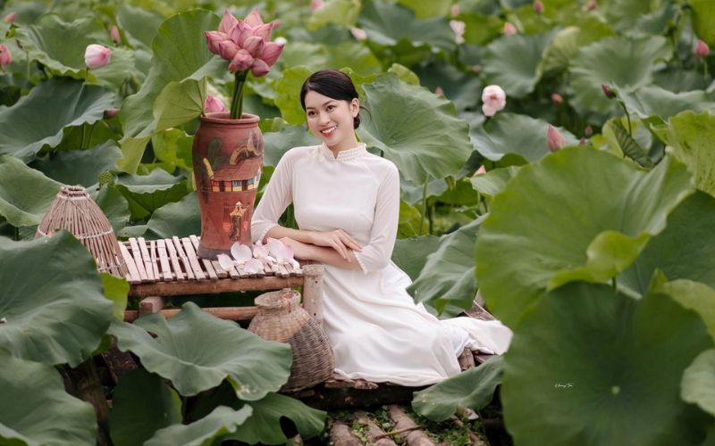 A girl wearing a traditional Vietnamese dress for Tet sits by a lotus pond, looking graceful.